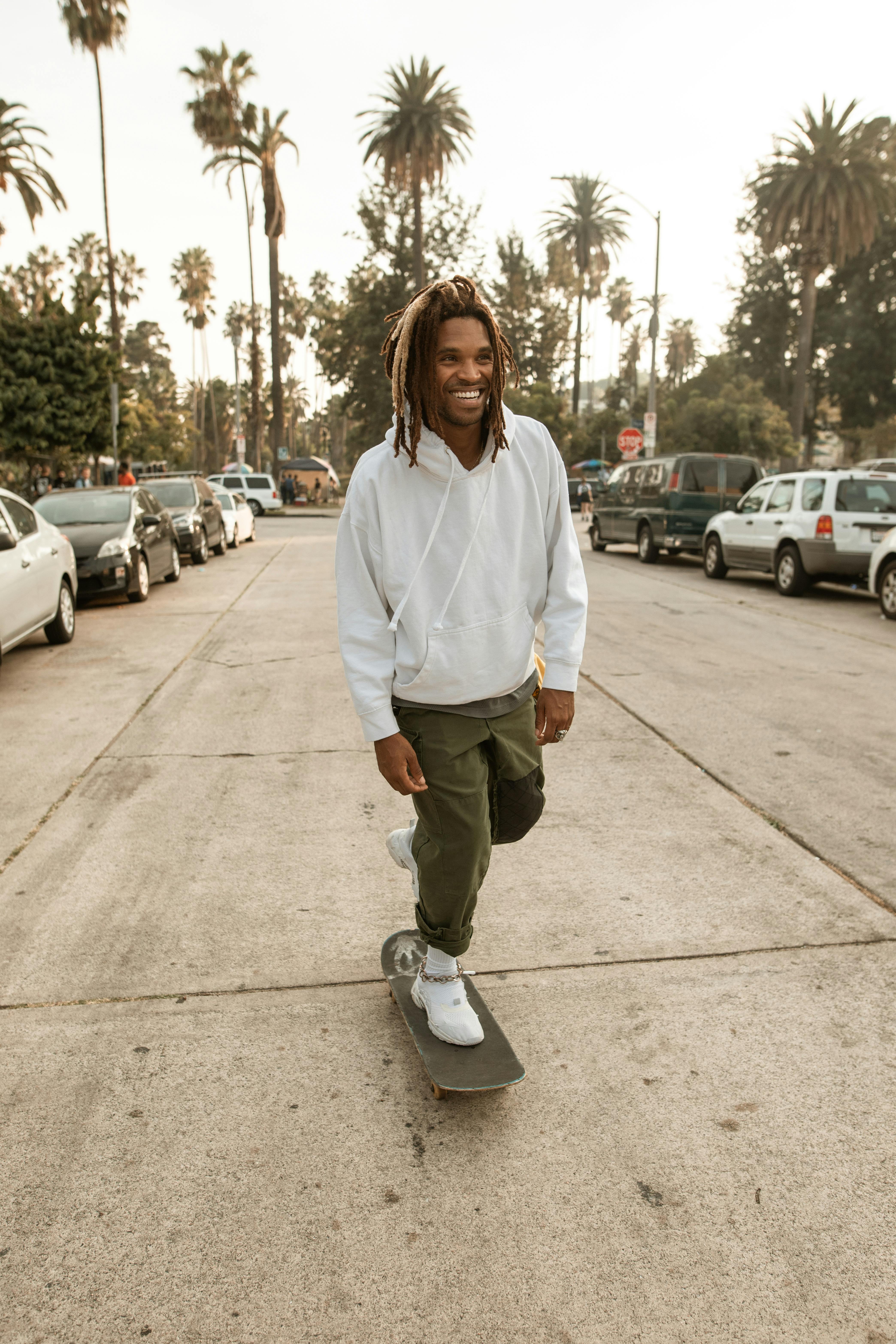Young man skateboarding on a sunny street lined with palm trees, exuding a relaxed and joyful vibe.