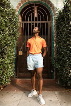 Fashionable man stands in front of a decorative doorway, surrounded by greenery.