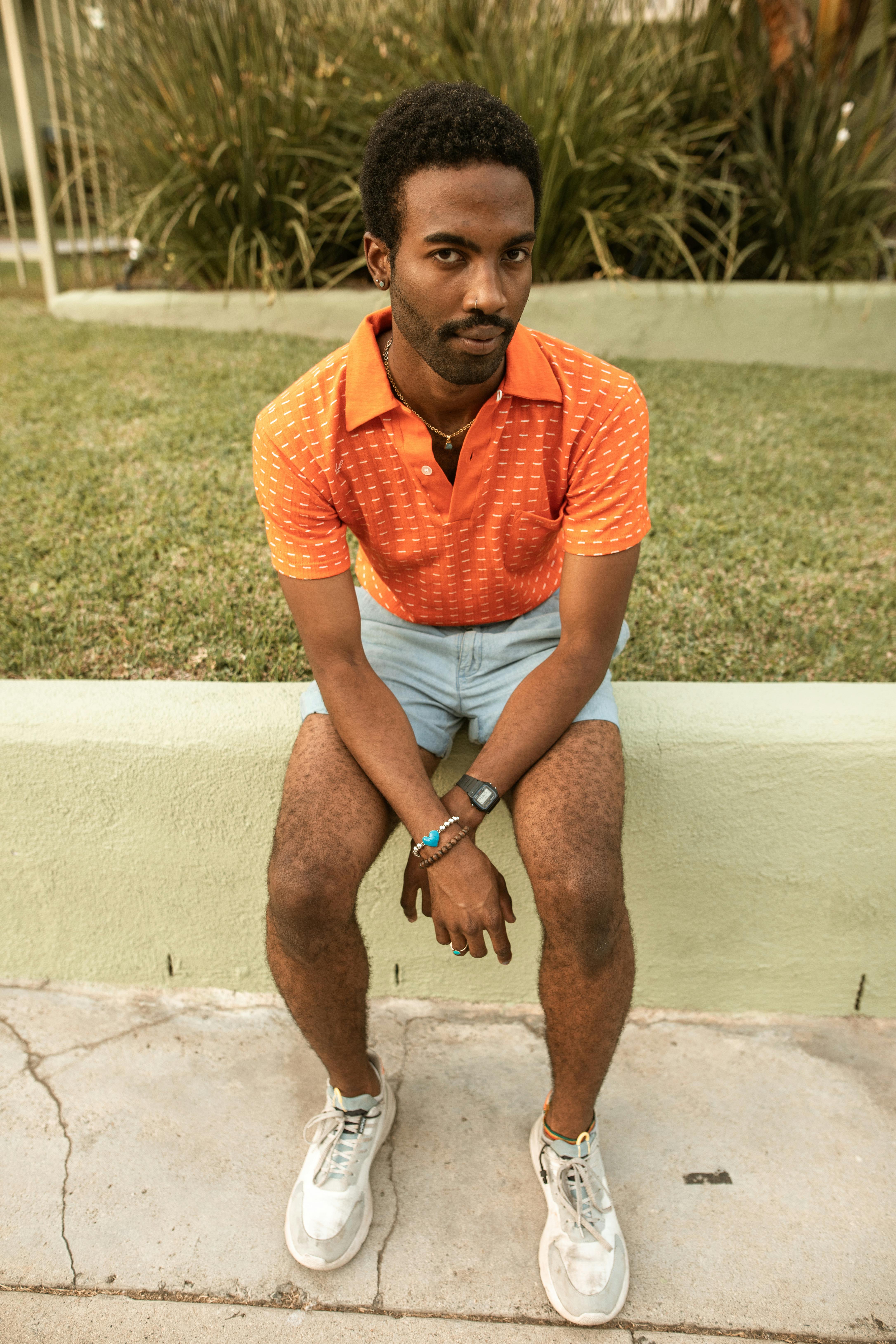 man in orange polo shirt and blue denim shorts sitting on white concrete bench