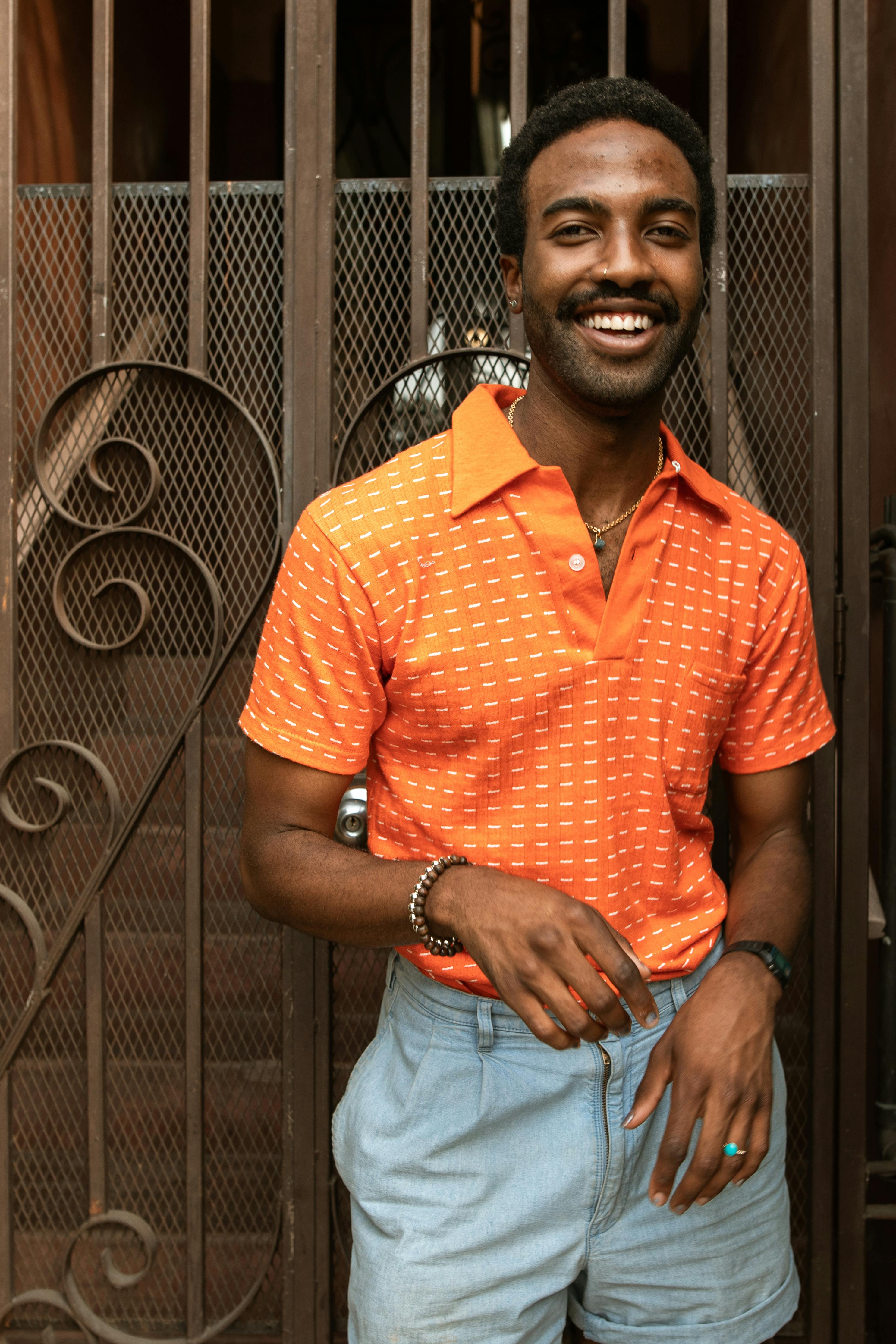 man in orange polo shirt and blue denim jeans standing beside black steel gate