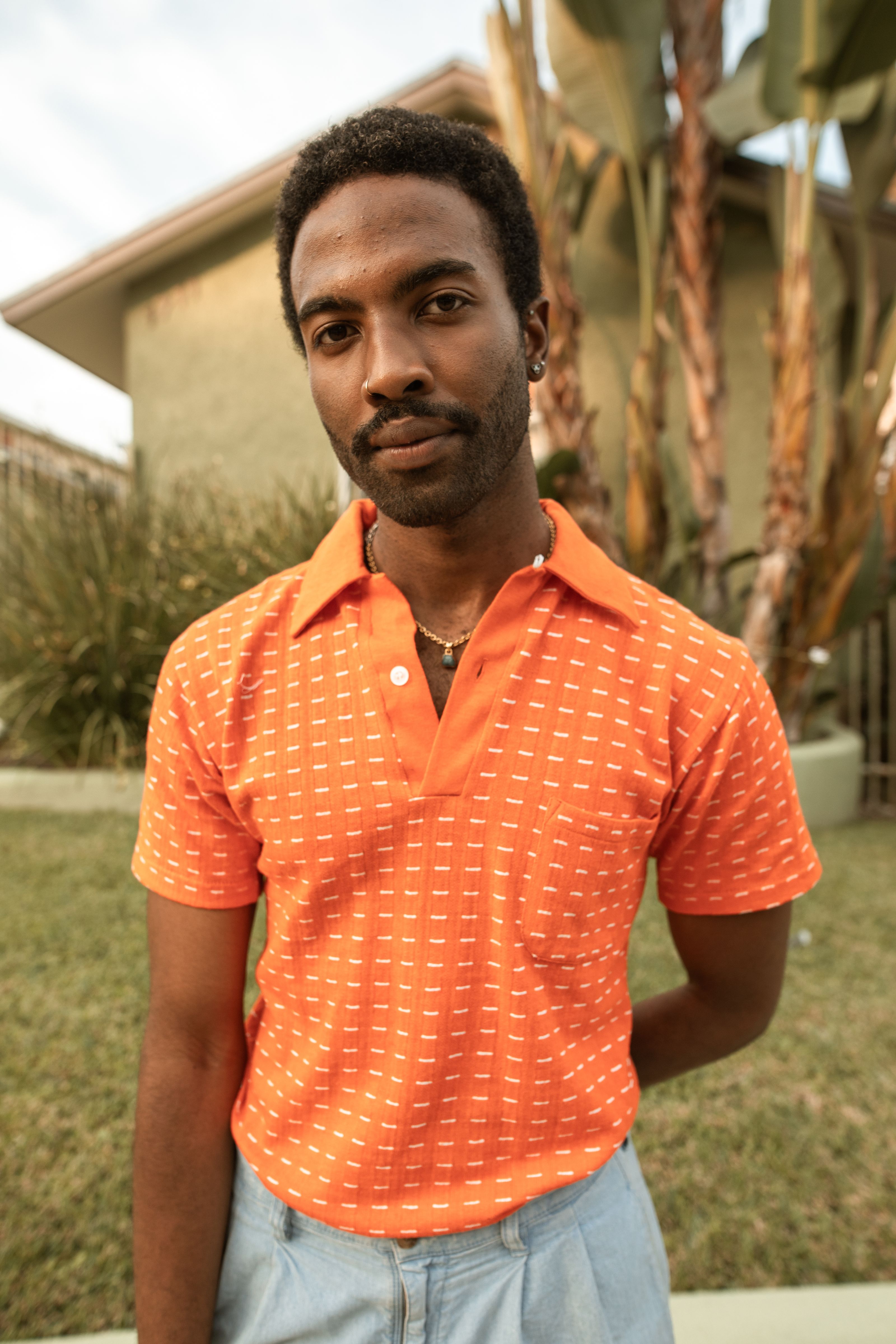Homem em uma camisa polo laranja posando ao ar livre com fundo natural.