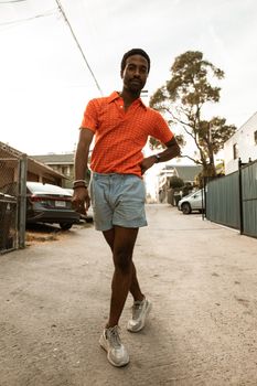 Confident man posing in urban alley, wearing trendy summer outfit.