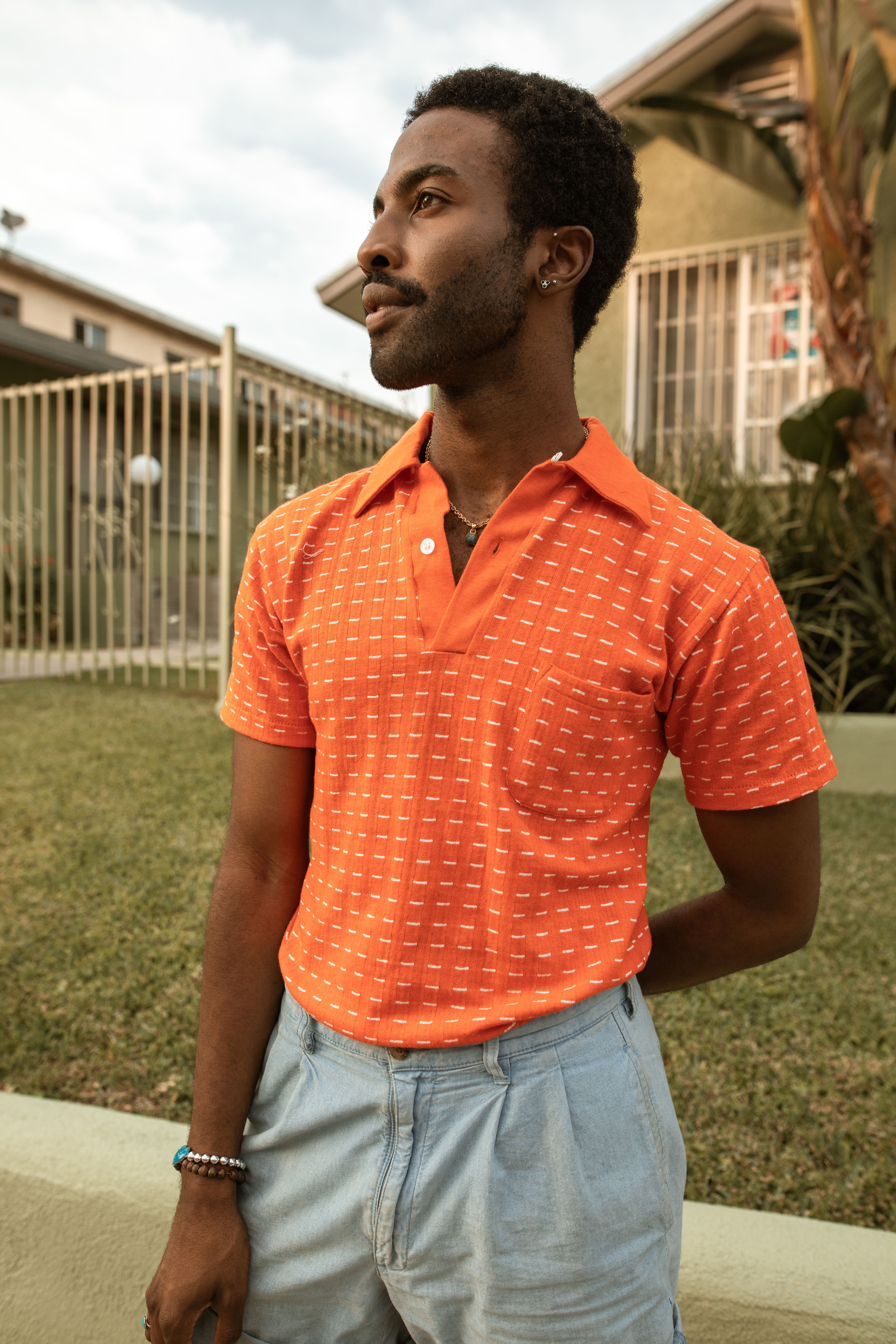 Confident man in a vibrant orange polo shirt posing outdoors.