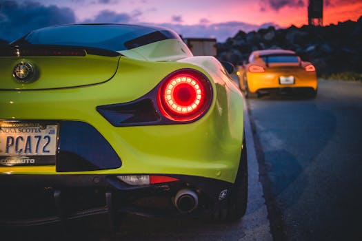 Expensive modern sports cars with red tail lights driving on asphalt road at sunset