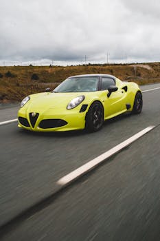 Yellow sports car driving fast on open road under cloudy sky.
