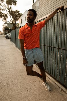 Young man in stylish orange polo shirt poses casually on a city street.