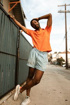 Stylish man in orange shirt and denim shorts posing confidently outdoors.