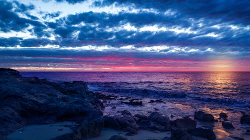 Rocky Shore Under Blue and White Cloudy Sky