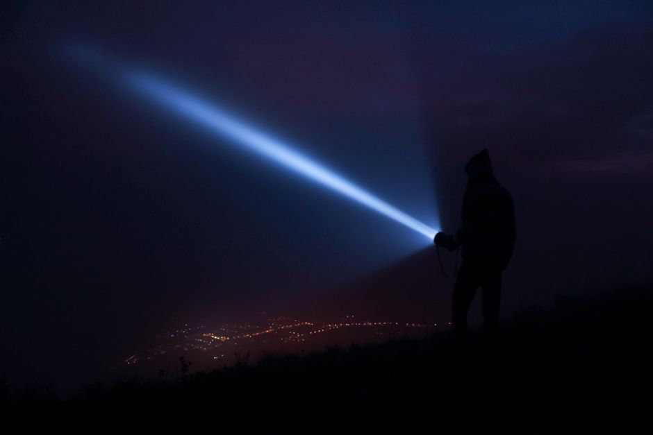 person holding flashlight in dark room at night