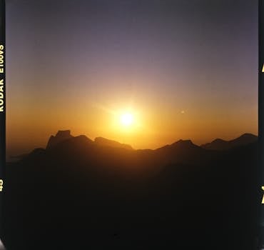 Film picture of bright sun rising above black silhouette of mountains in early morning