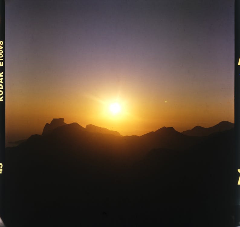 Film picture of bright sun rising above black silhouette of mountains in early morning