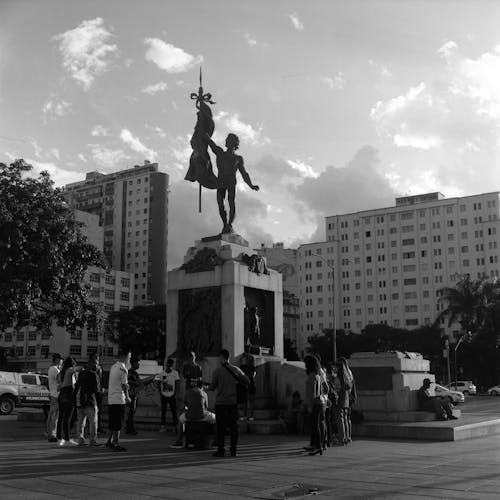 Black and white tourists exploring monument with male statue in modern city district