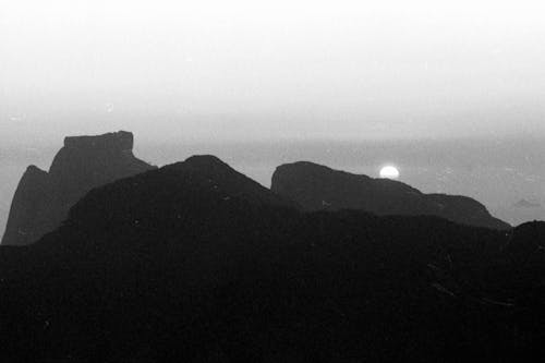 Monochrome scenery of black silhouette of rocky mountains against dull sky with sunset