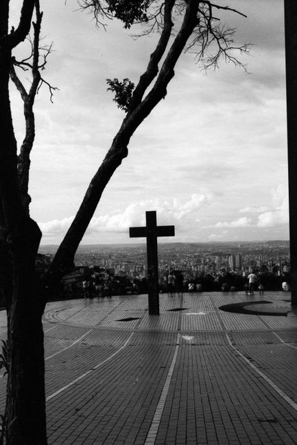 Black and white of high viewpoint in city with people walking on paved square with cross sculpture