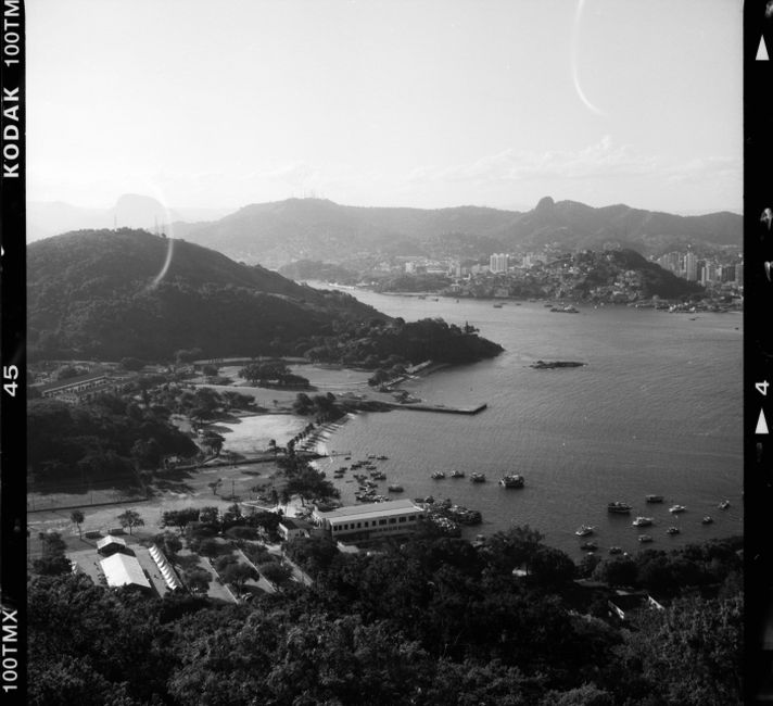 Monochrome film shot of seashore with small settlement and docks among mountains in sunlight