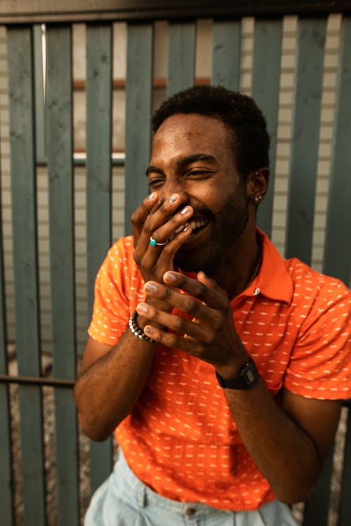 Man in Orange Shirt Laughing with Hands on Mouth