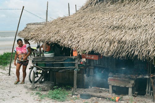 Ethnic woman walking at small hut with thatched roof in local poor village on ocean shore