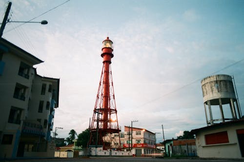 From below of red metal tower of lighthouse in urban dock with industrial buildings around