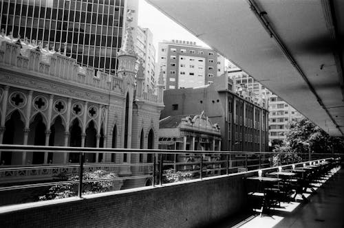 Black and white of narrow balcony terrace with rows of tables against new and old buildings of city