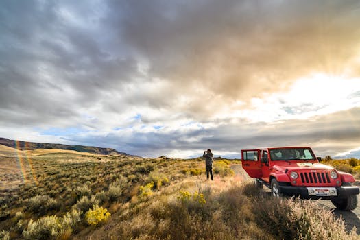 Person photographing with red SUV in open landscape, epitomizing travel freedom.