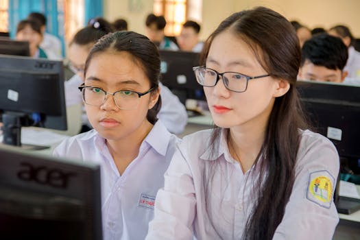 Two female students in a classroom focusing on computer work, showcasing education and technology.