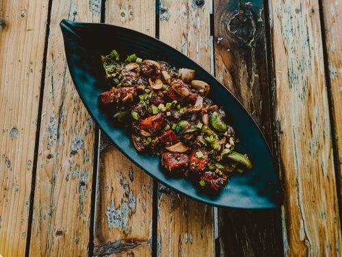 Free Gourmet food served on a black leaf-shaped plate atop a rustic wooden table, offering a vibrant culinary experience. Stock Photo
