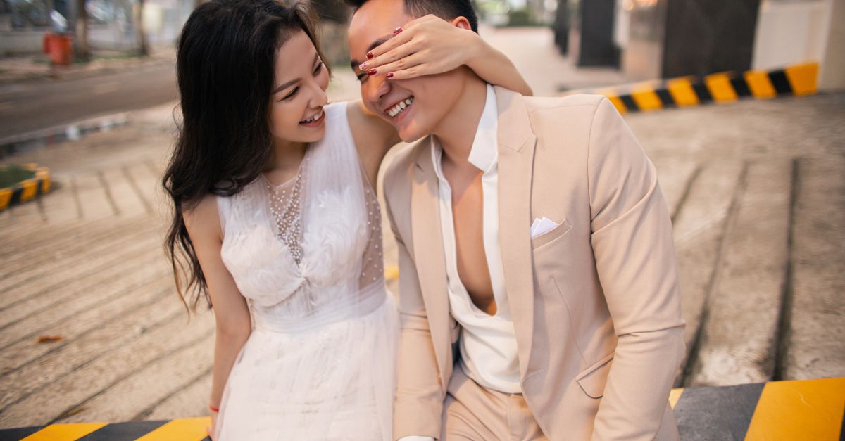 Happy Asian newlyweds laughing together outdoors on a sunny day.