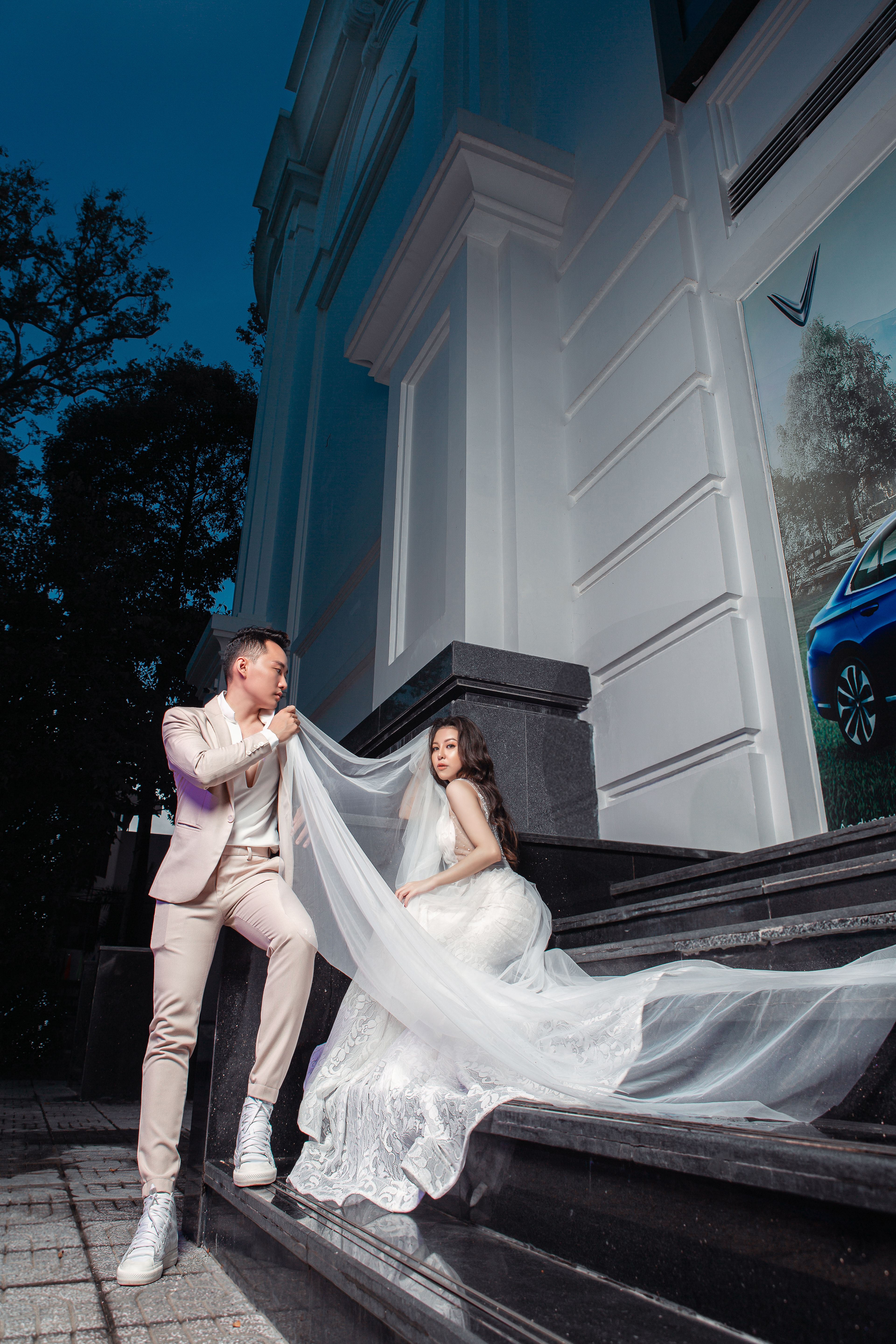 Stylish couple poses in wedding attire on a modern building's steps creating a timeless urban scene.
