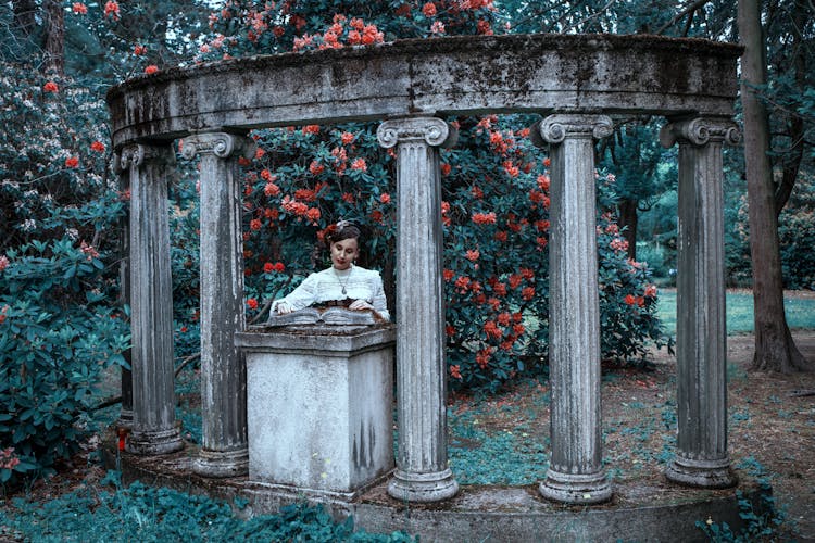 A Woman Standing Near Pillars And Green Plants With Orange Flowers While Looking At The Camera