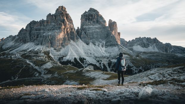 A hiker admires the majestic Tre Cime di Lavaredo in the Italian Dolomites, perfect for travel enthusiasts.