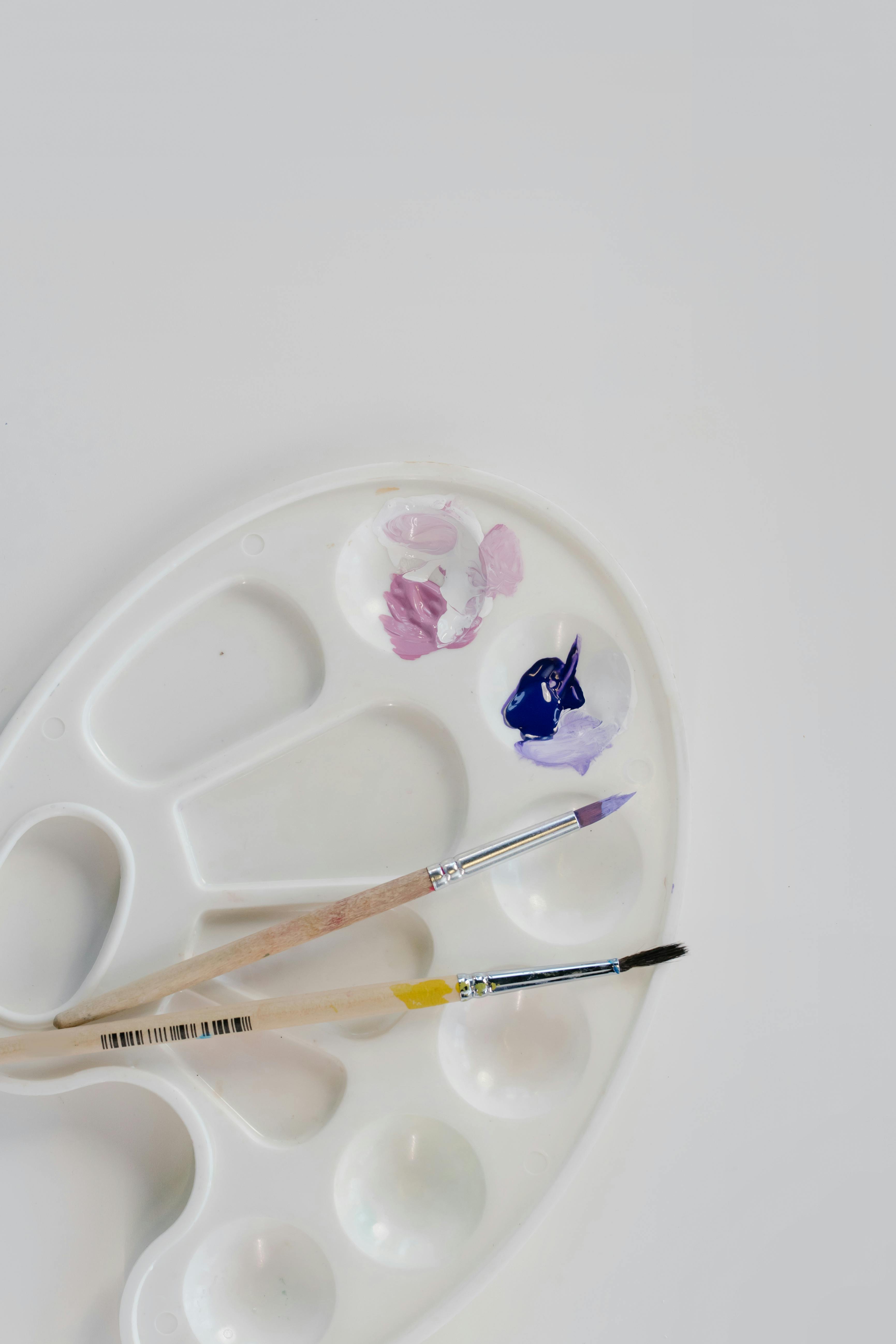 Close-up of an art palette with paintbrushes and vibrant colors on a white background.