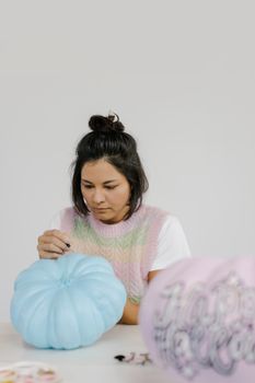 一名女子为万圣节室内手工项目，创意性地绘制了一个柔和的蓝色南瓜