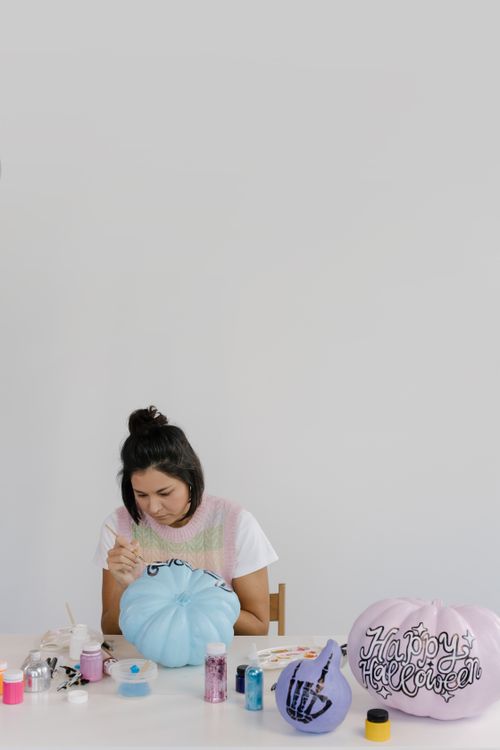 Free Woman painting pumpkins indoors for creative Halloween decorations. Stock Photo
