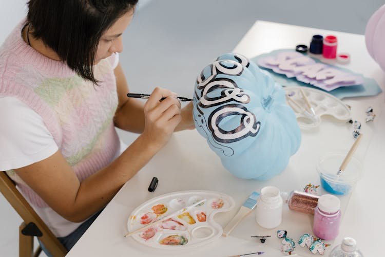 Woman Holding A Black Marker Drawing On A Blue Pumpkin 