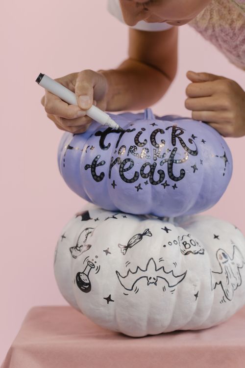 Free A person decorates stacked pumpkins with Halloween-themed designs and text. Stock Photo