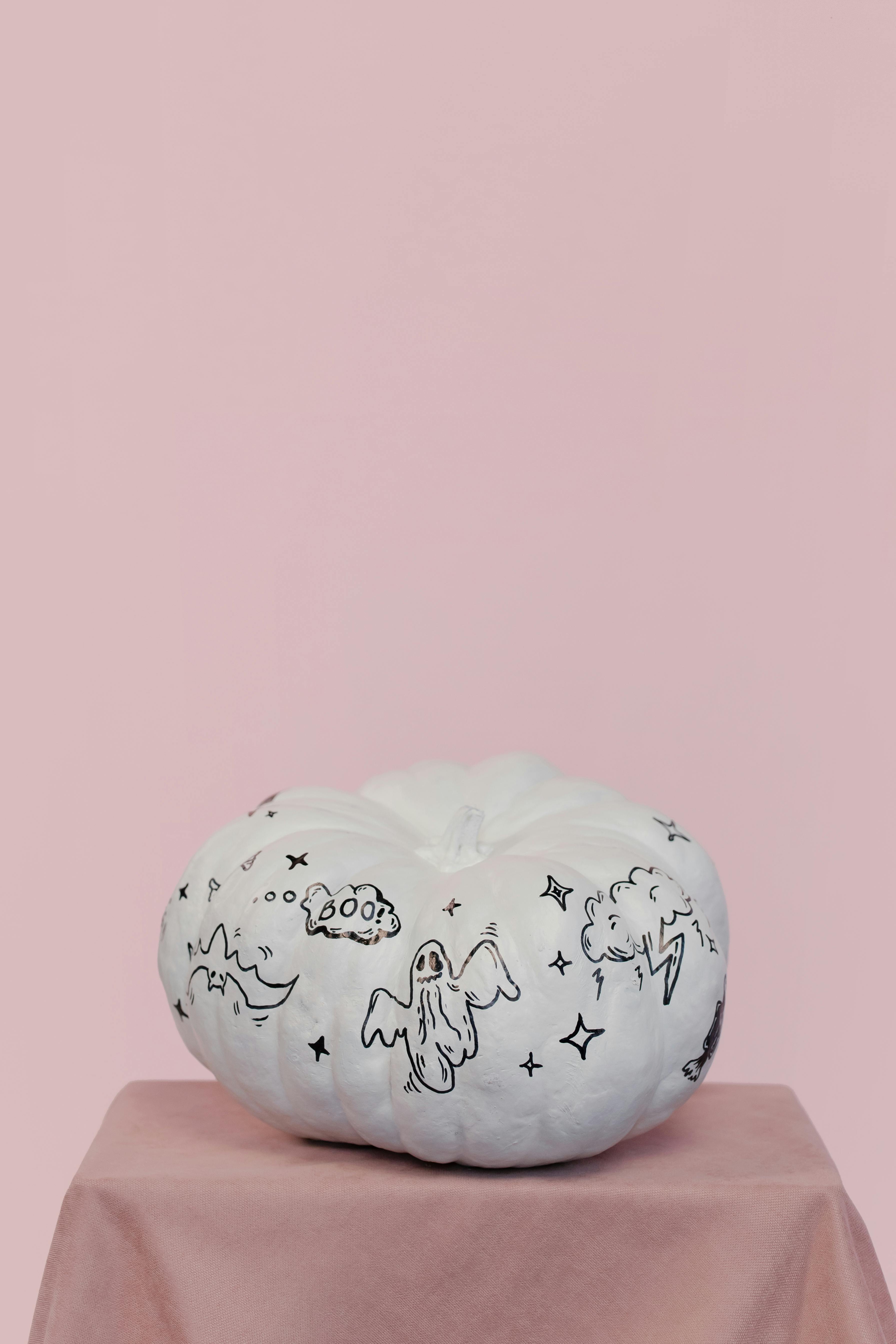 白色南瓜上绘有万圣节图画，置于柔软的粉红色背景之上，非常适合节日装饰
