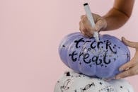 粉红色背景上，装饰着蓝色万圣节南瓜的双手特写，上面写着“不给糖就捣蛋”