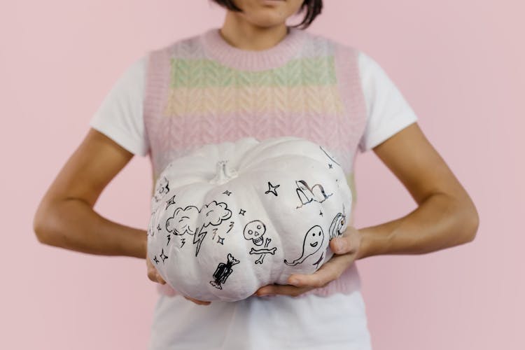 A Person Holding A White Pumpkin With Spooky Drawings