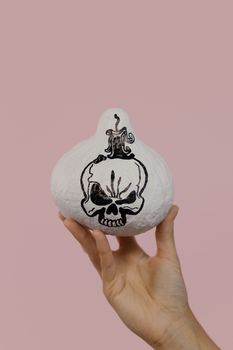 一只握着南瓜的手的特写，南瓜上画着骷髅头，背景是粉红色，非常适合万圣节主题