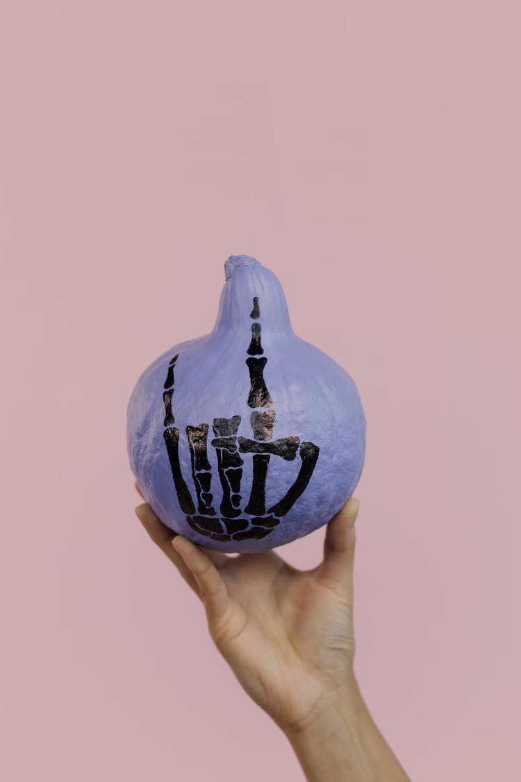 A Hand Holding Purple Halloween Pumpkin On A Pink Background