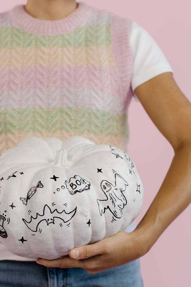 A Person Holding A White Pumpkin With Scary Drawings