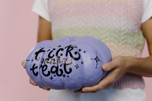 Free Close-up of a person holding a lavender pumpkin with 'trick or treat' text, perfect for Halloween decoration. Stock Photo