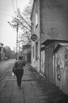 Black and white urban scene of a street in Łódź, Poland, capturing a solitary figure walking.
