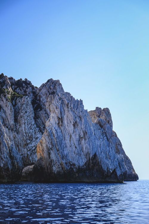 Free Breathtaking view of rough rocky formation in calm ocean water under clear blue sky Stock Photo