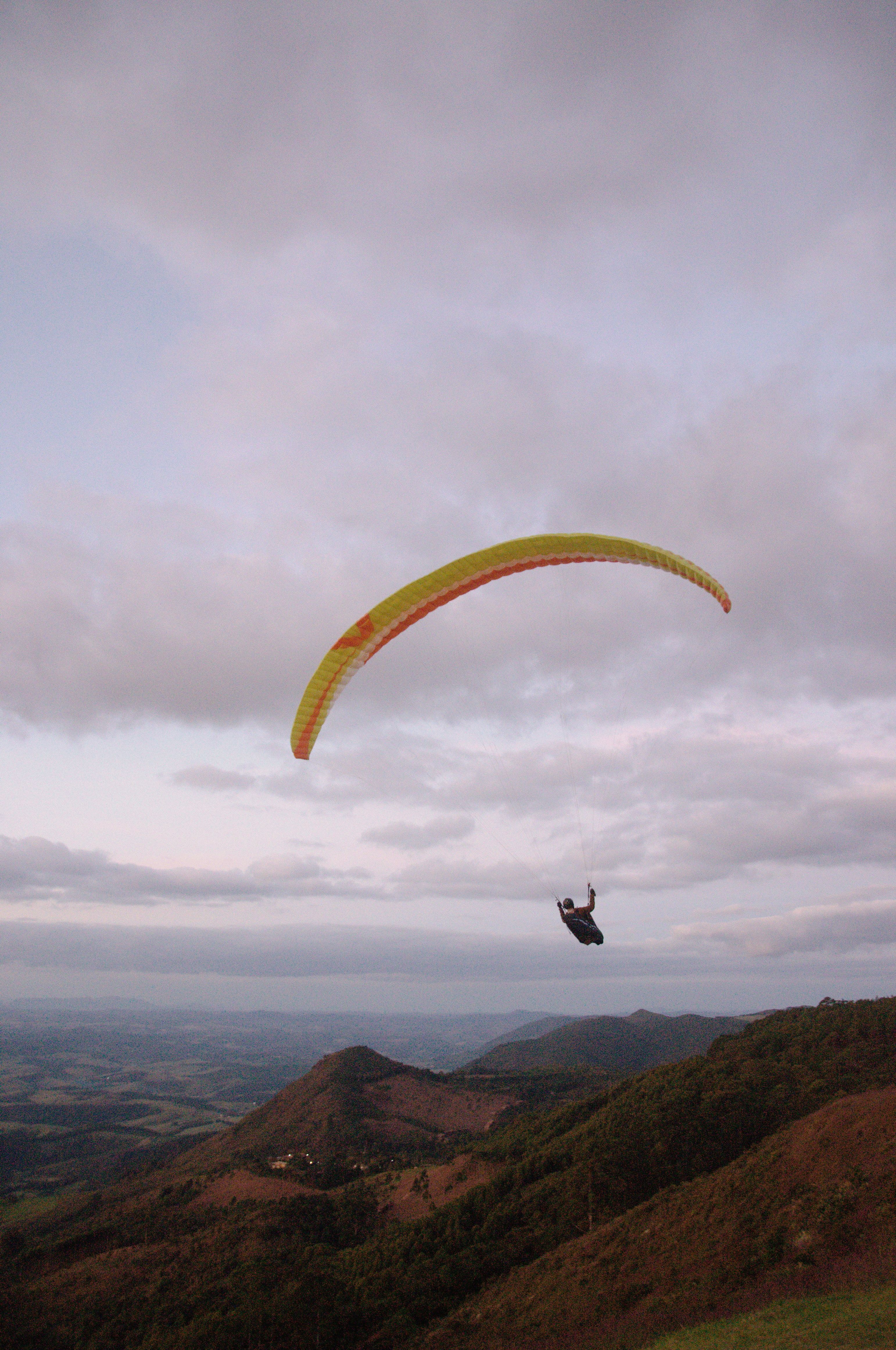 A paraglider gracefully glides over stunning mountainous terrain with a cloudy sky backdrop.