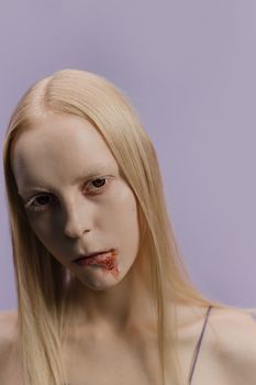 在紫色背景下，一位苍白金发的女子肖像令人毛骨悚然，她的嘴唇沾满血迹