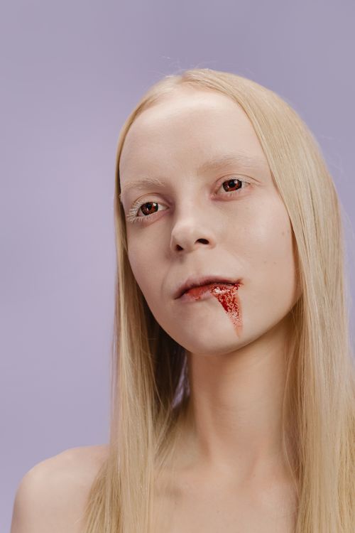 Free Studio portrait of an ethereal woman with blonde hair and a blood stain, creating a striking and eerie atmosphere. Stock Photo