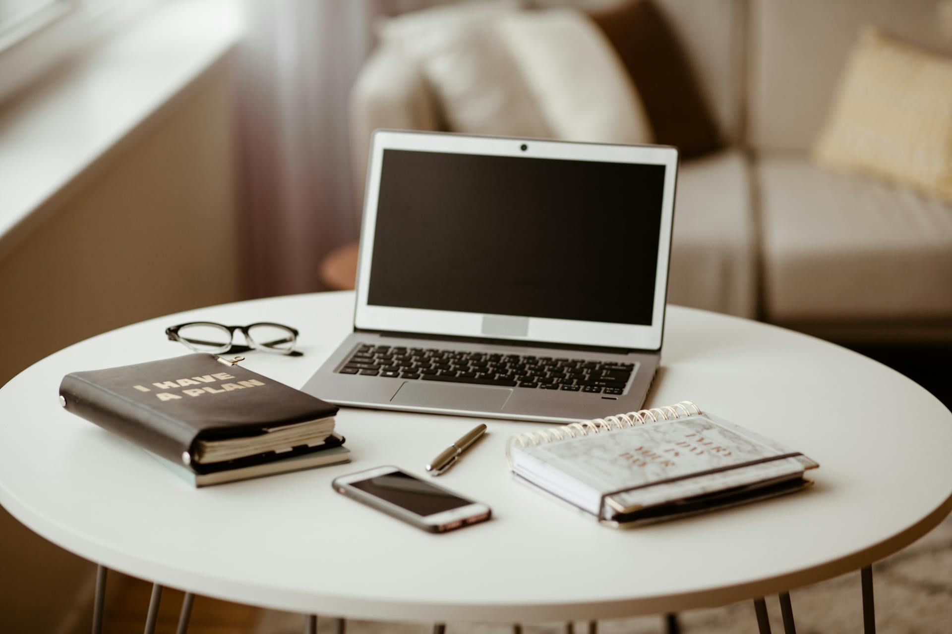 A cozy home office setup featuring a laptop, planner, and eyeglasses on a round table.