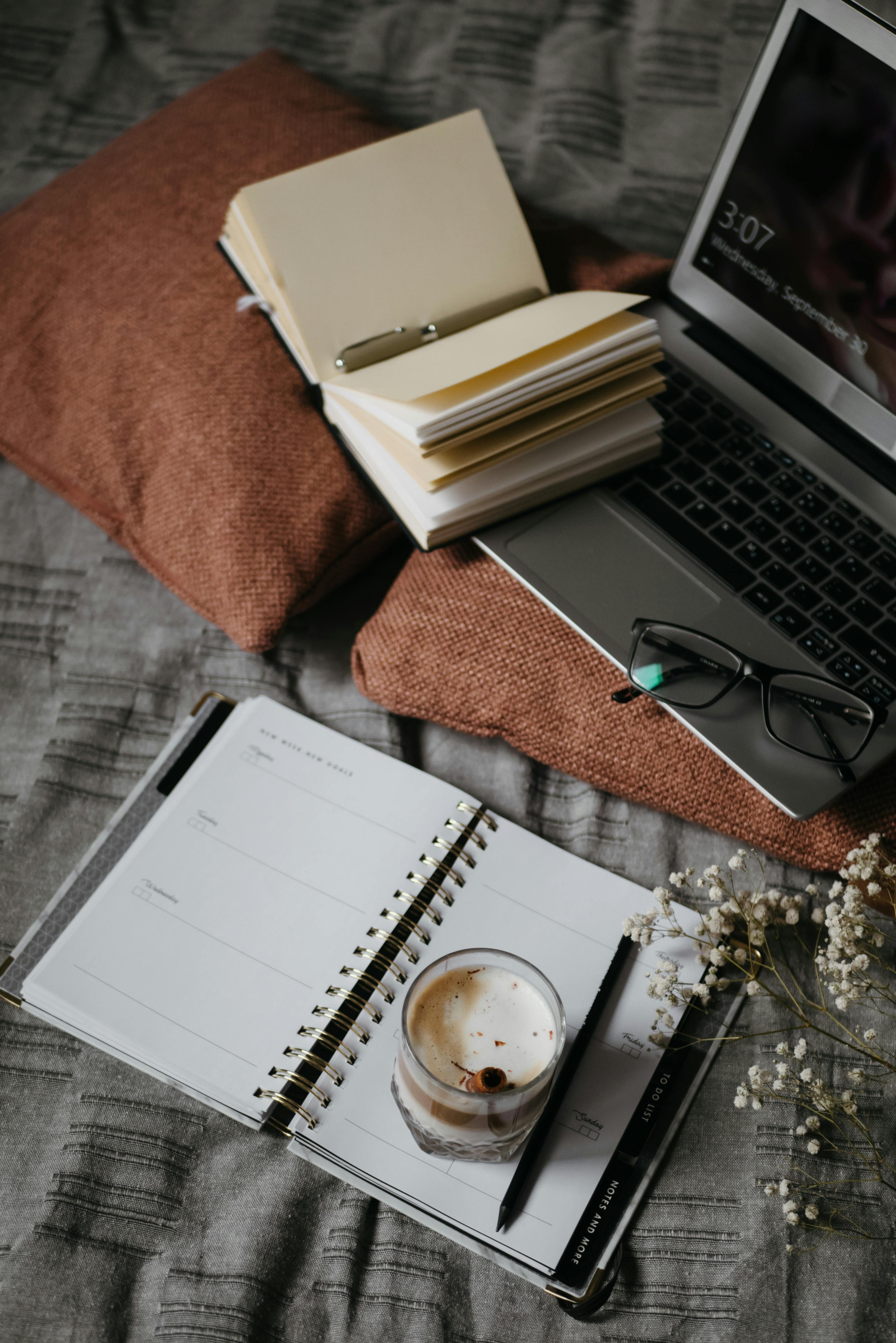 black and silver laptop computer beside white notebook and black framed eyeglasses