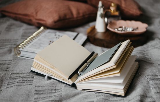 Open notebook with pen on a cozy bedspread surrounded by accessories, perfect for writing inspiration.
